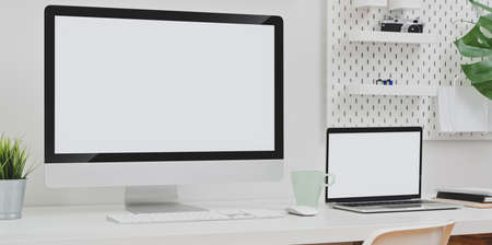 Desktop computer and blank screen laptop with copy space and office supplies in minimal white office roomの写真素材