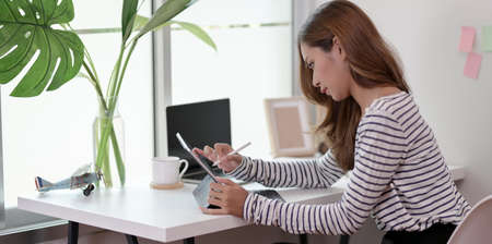 Professional young designer editing her project on tablet in her comfortable workplaceの写真素材