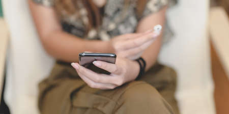 Close-up view of female holding smartphone and earphone in comfortable roomの写真素材
