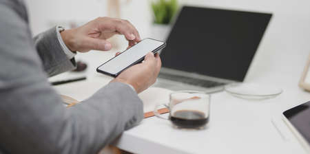 Close-up view of businessman touching blank screen smartphone in his modern office roomの写真素材