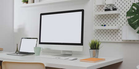 Desktop computer and blank screen laptop with copy space and office decorations in minimal white office roomの写真素材