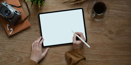 Top view of female hand writing on blank screen tablet on modern rustic table background with vintage cameraの写真素材