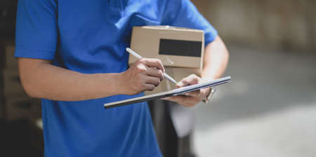 Professional delivery man working with parcel box while checking customer order on tablet.の写真素材
