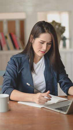Professional female freelancer working on her project while writing on notebook in modern workplaceの写真素材