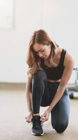 Young slim fitness girl doing shoelaces in the sport gym, preparing before running inside the gymの写真素材