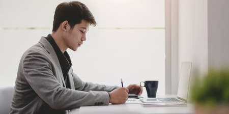 Young professional businessman writing his plan on notebook while working on the project.