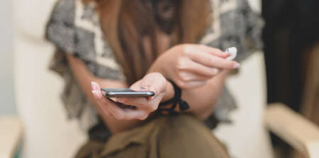Close-up view of female holding smartphone and earphone in comfortable roomの写真素材