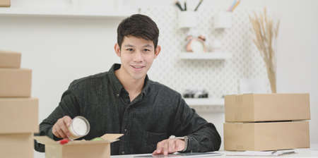 Young male small business owner preparing and packaging the products for customers at home and smiling to the cameraの写真素材