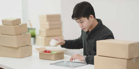 Small business concepts : Young male owner packing and selling online products at homeの写真素材