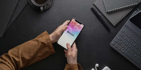 CHIANG MAI, THAILAND - AUGUST 30, 2019 : female hand holding iPhone with Apple Music app on dark stylish workplace. Apple Music is the new iTunes-based music streaming service that arrived on iPhoneのeditorial素材