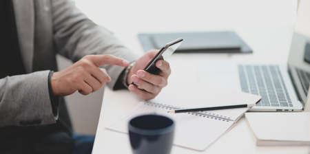 Cropped view of young businessman touching his smartphone in comfortable roomの写真素材
