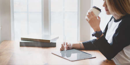 Beautiful professional freelancer working on her project with tablet while having a cup of coffee