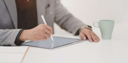 Close-up view of young businessman writing his ideas on blank screen tablet in comfortable room