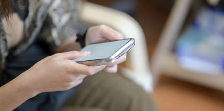Close-up view of young female holding blank screen smartphone while sitting on the chair