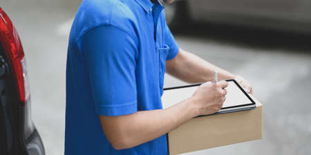 Close-up view of young delivery man checking the products to customer while standing right next to his car.の写真素材