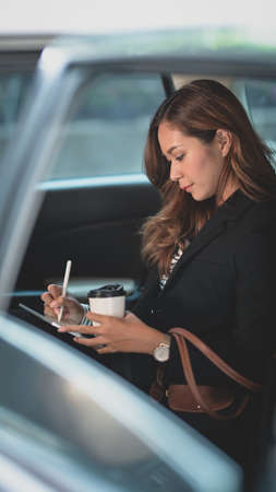 Beautiful businesswoman sitting at the back set of the car while heading to the officeの写真素材