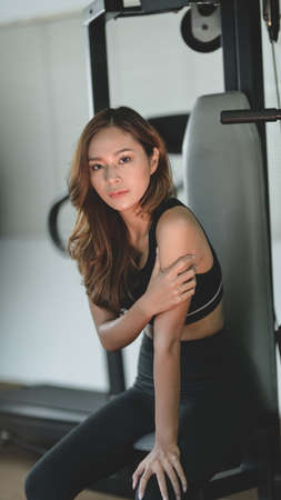 Beautiful young asian woman sitting on the weight-lifting machines in the modern gymの写真素材