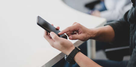 Close-up of young professional businessman touching his smartphone in modern officeの写真素材