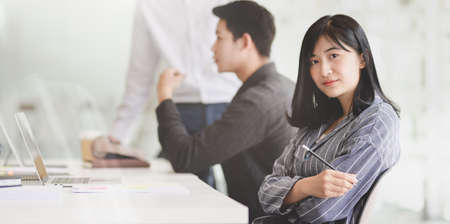 Beautiful young businesswoman sitting in the meeting room with her team members discussing in the backgroundの写真素材
