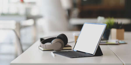 Modern workplace with blank screen tablet, on-ear headphones and office supplies on white tableの写真素材