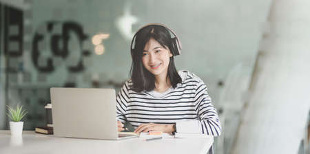 Young female freelancer working on her project with laptop computer while listening to her favourite music with headphonesの写真素材
