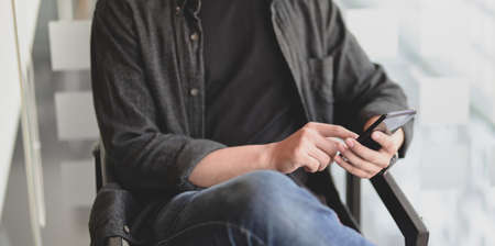 Close-up of young professional businessman holding and looking at smartphone in modern officeの写真素材