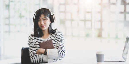 Young adorable female holding a book while listening to her favourite music in workplaceの写真素材