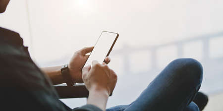 Close-up of young professional businessman looking for informations at smartphone in modern officeの写真素材