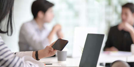 Young female freelancer looking for information on smartphone with her team members in the backgroundの写真素材