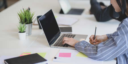 Cropped shot of young businesswoman working on her recent project with laptop computer and writing some idea on notebookの写真素材