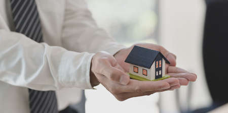 Property insurance concept : insurance agent holding a house model in his hand, symbol of home insuranceの写真素材