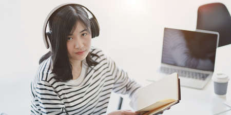 Young adorable female freelancer working on her project while listening to music and looking at the cameraの写真素材