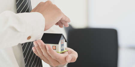 Property insurance concept : insurance agent holding a house model in his hand, symbol of home insuranceの写真素材