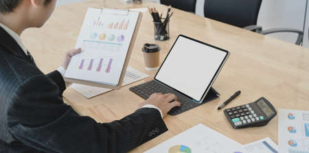 Close-up view of young businessman working on his current project while using tablet and charts