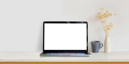 Open blank screen laptop computer on white wooden table in white minimal workplace with coffee cup and vaseの写真素材