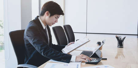 Male accountant analysing and reviewing expenditures for his company in the office roomの写真素材