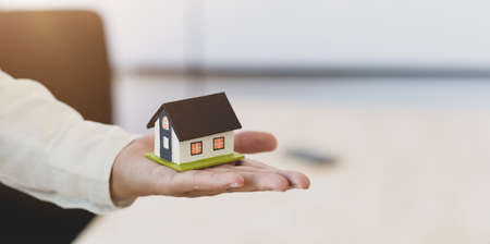 Businessman holding a house model in one hand, symbol of home insuranceの写真素材