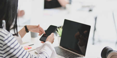 Young female freelancer working on blank screen smartphone with her team members in the backgroundの写真素材