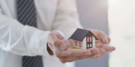 Property insurance concept : insurance agent holding a house model in his hand, symbol of home insuranceの写真素材