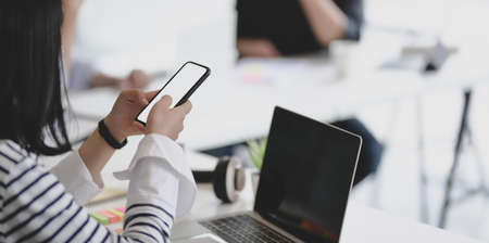 Young female freelancer working on blank screen smartphone with her team members in the backgroundの写真素材