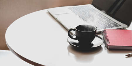 Minimal workplace with open laptop, coffee cup and office supplies on white tableの写真素材