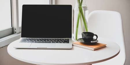 Minimal workplace with open laptop, coffee cup and office supplies in comfortable cornerの写真素材