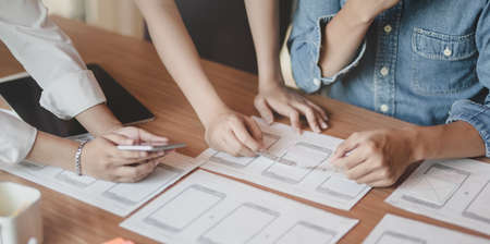 Team of young professional UI graphic designer discussing on their smartphones templates togetherの写真素材