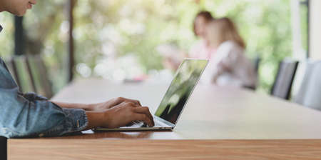 Young UX web developer working on the smartphone templates on laptop computer with his coworkers in the backgroundの写真素材