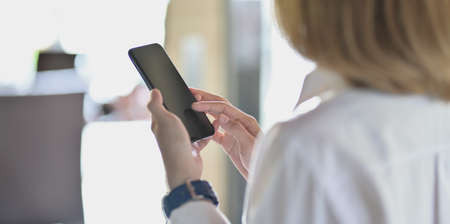 Young businesswoman looking for new informations on smartphone with blurred office backgroundの写真素材