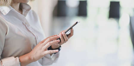Close-up view of young businesswoman holding smartphone with blurred office backgroundの写真素材