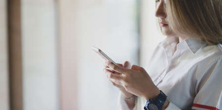 Close-up view of young businesswoman looking for new informations on smartphone with blurred office backgroundの写真素材