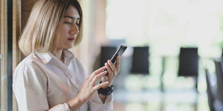 Young businesswoman looking for new informations on smartphone with blurred office backgroundの写真素材