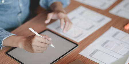 Close-up view of male UI web developer working on his smartphone templates with blank screen tablet in modern officeの写真素材