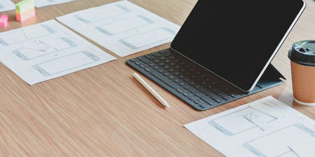 Cropped shot of UX web developer workplace with tablet and a cup of coffee on wooden table in comfortable roomの写真素材